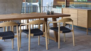 Un comedor moderno con una larga mesa de madera, cuatro sillas y lámparas colgantes.