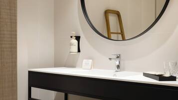 Un baño moderno con un espejo redondo, un lavamanos blanco, un mueble de tocador negro y un perchero para toallas.