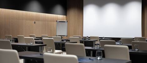 A conference room with tables, chairs, a projector screen, and a whiteboard.