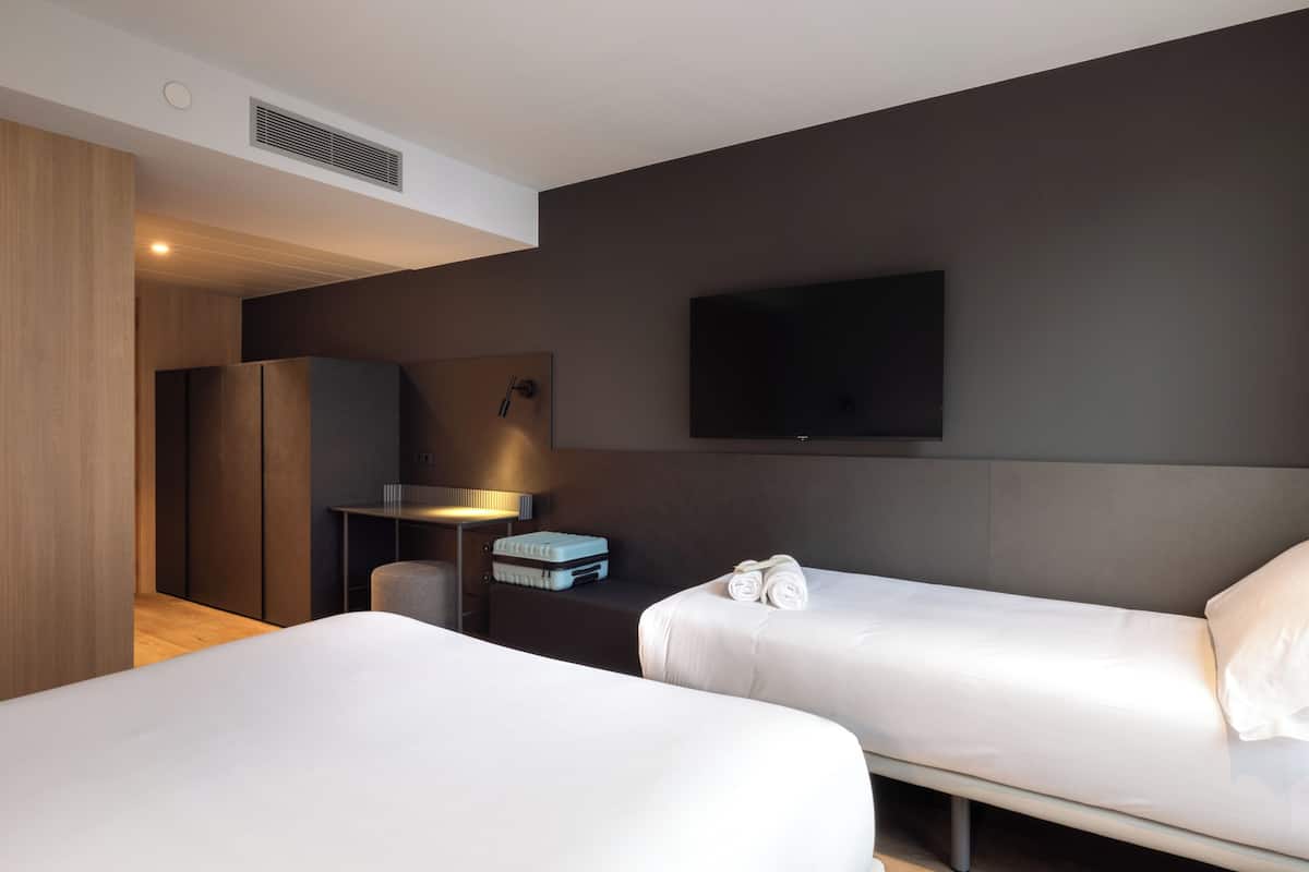 A modern hotel room with two beds, a desk, a flat-screen TV, and a wardrobe.