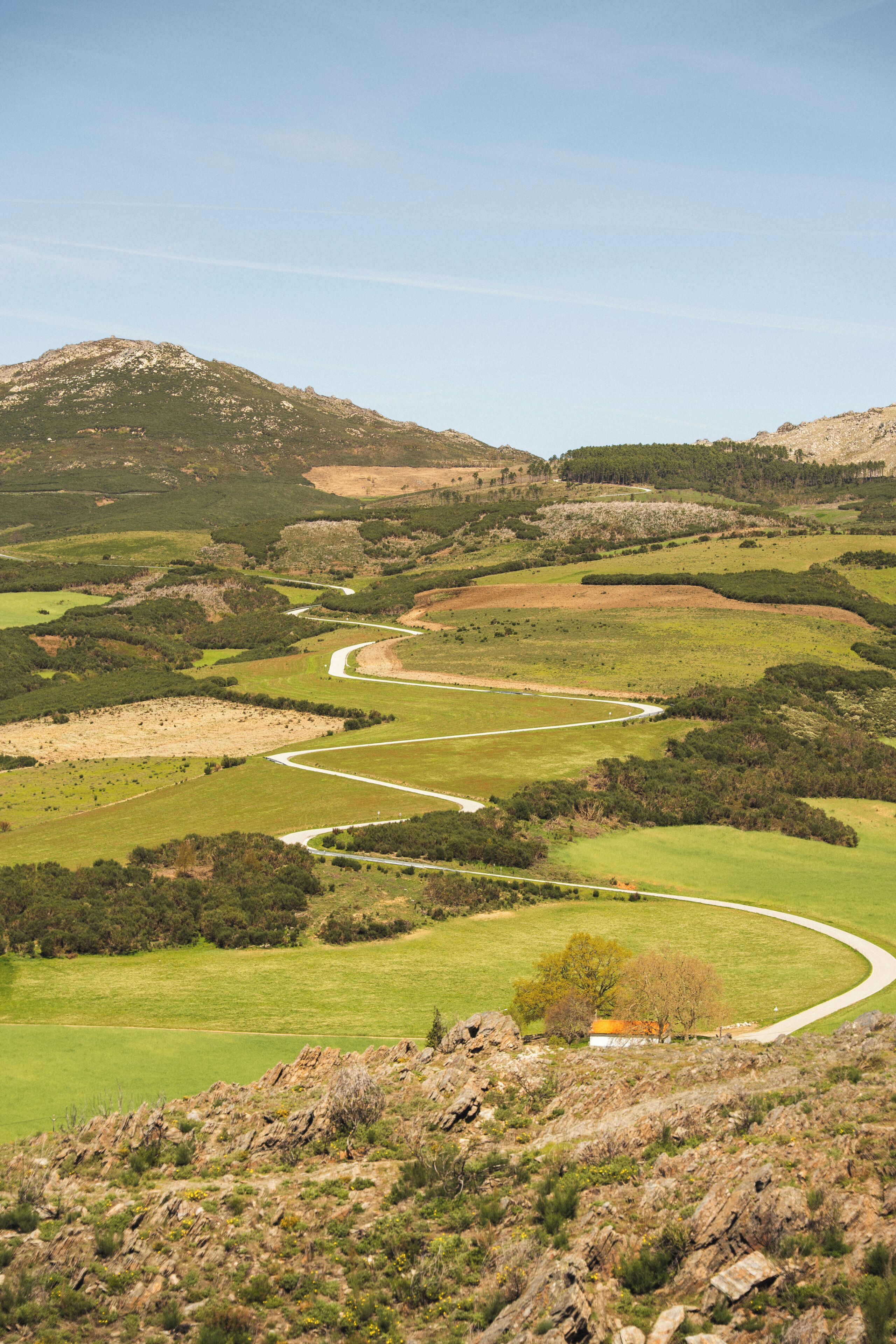 A winding road through a hilly landscape with green fields and rocky outcrops.