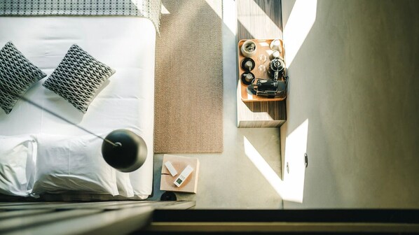 A neatly made bed with pillows, a bedside table with a lamp, a tray with cups and a camera, and a wall-mounted light fixture. - TerraSense Mountain Charm Retreat & Farm (Guarda)