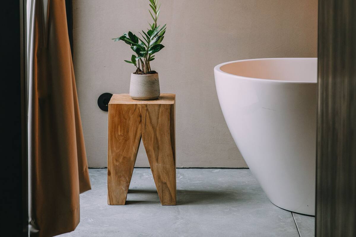 Une salle de bain avec une grande baignoire, un petit tabouret en bois sur lequel est posée une plante en pot, et un rideau.