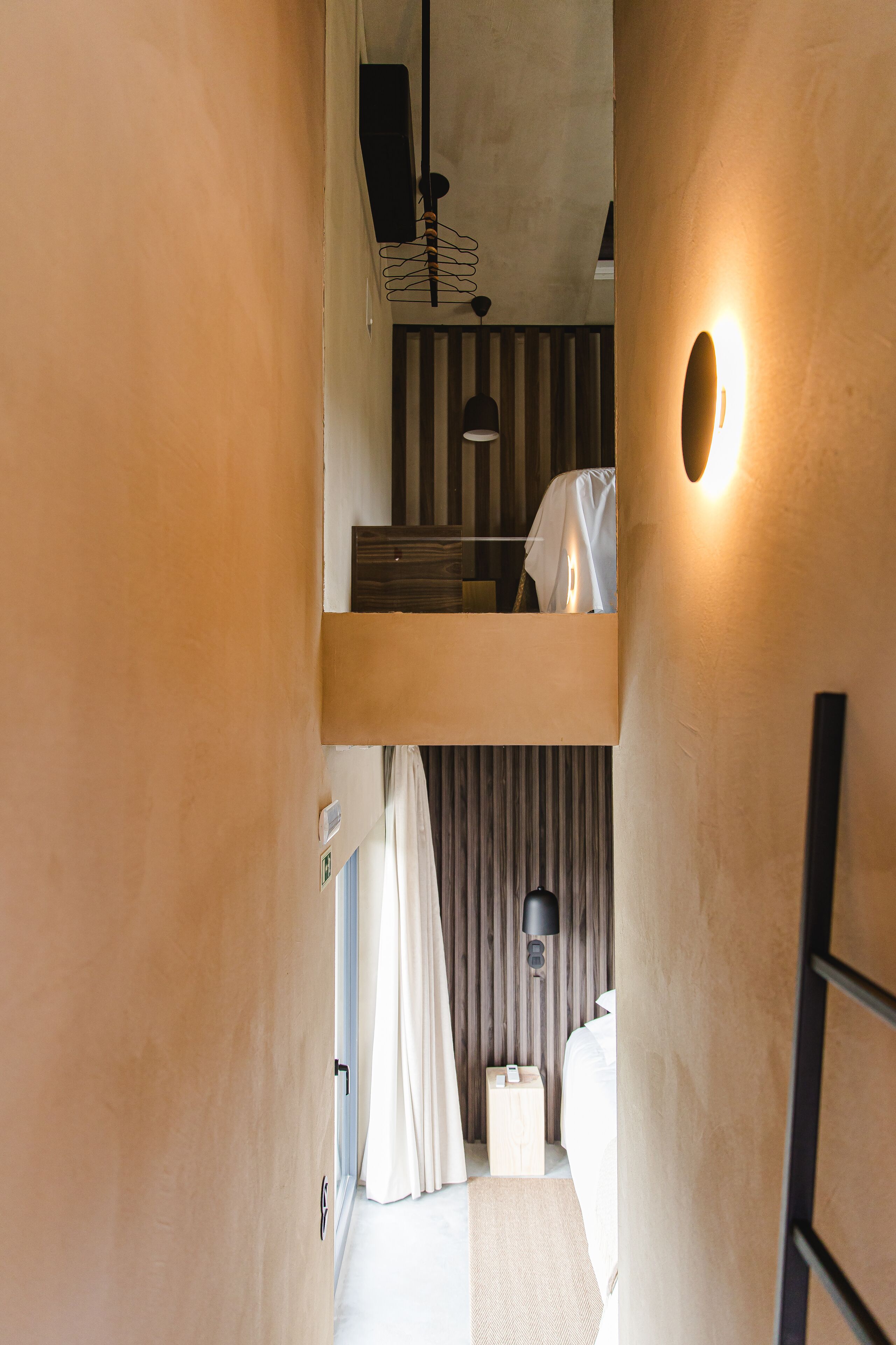 A narrow hallway leading to a bedroom with a bunk bed, a bedside table, a lamp, and a curtain.