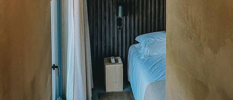 A compact room with a loft bed, a bedside table, a lamp, and a curtain.
