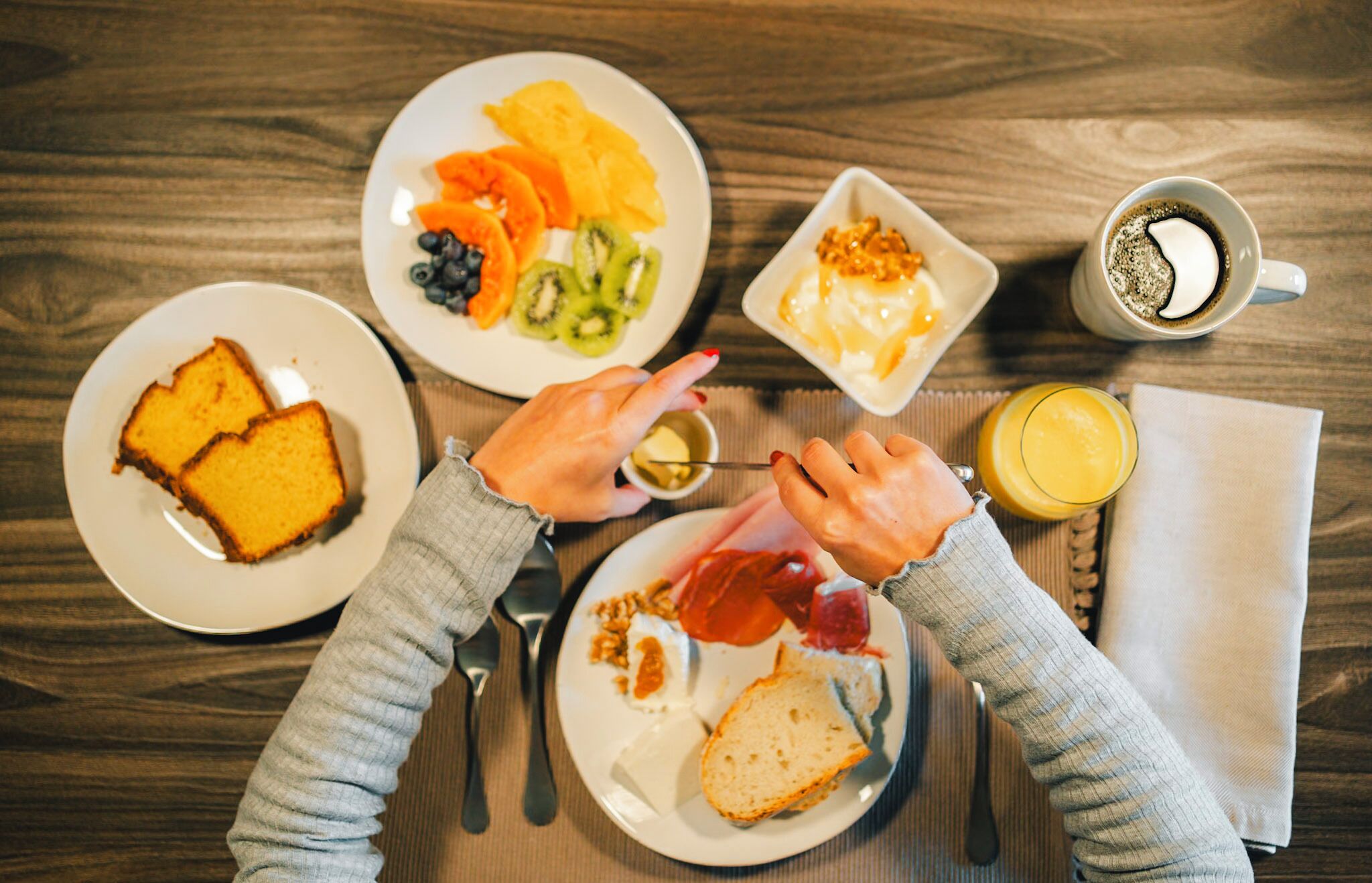 Uma mesa de madeira com torradas, frutas, ovos, utensílios e uma xícara de café para o café da manhã.