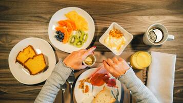 Uma mesa de madeira com torradas, frutas, ovos, utensílios e uma xícara de café para o café da manhã.