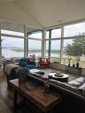 A spacious living room with a large window offering a view of a body of water and hills.