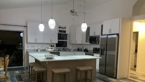 A modern kitchen with white cabinets, a stainless steel refrigerator, a large island with bar stools, and pendant lighting.