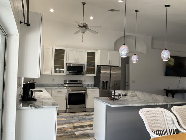 A modern kitchen with white cabinets, stainless steel appliances, a marble countertop, and a ceiling fan. - Remodeled with pool/spa home in golf resort for rental! Very cool house! (Sebring)
