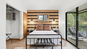 Une chambre à coucher avec un lit, des tables de chevet, un banc et une vue sur l’extérieur.