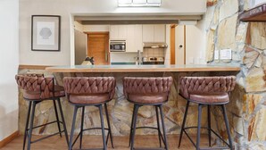 Une cuisine avec un mur en pierre, un coin bar avec des tabourets en cuir et un tableau encadré au mur.