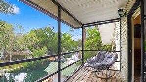 Un balcon donnant sur un plan d’eau et des arbres, une chaise grise et une petite table.