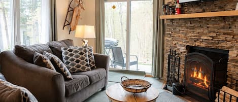 A cozy living room with a fireplace, a sofa set, and a stone wall.