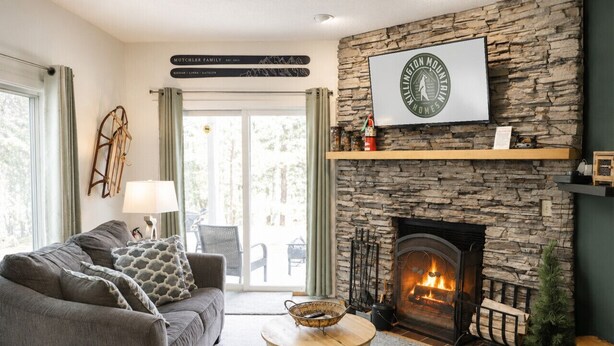 A cozy living room with a stone fireplace, a sofa set, and a dining table. - Bearmont- Pool, HotTub, FirePit, AC, Gym, Sauna (Killington)