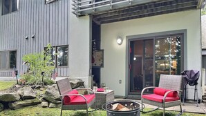A patio with two wicker chairs, a fire pit, and a small garden with rocks and plants. - Bearmont- Pool, HotTub, FirePit, AC, Gym, Sauna (Killington)
