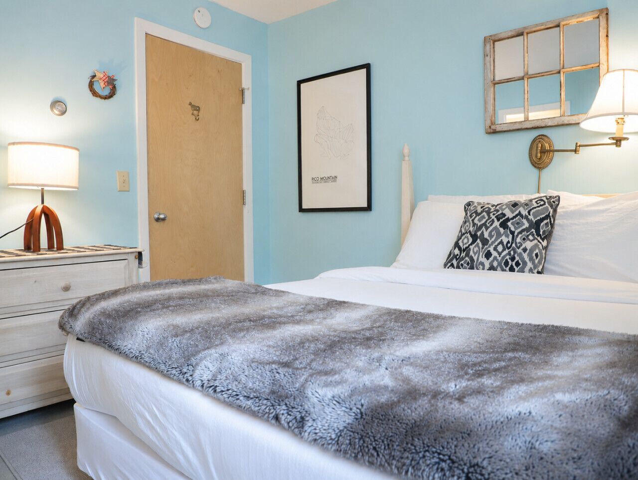 A bedroom with a bed, a bedside lamp, a framed picture, and a door.