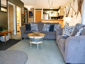 A living room with a grey sofa set, a wooden coffee table, and a kitchen in the background. - Bearmont- Pool, HotTub, FirePit, AC, Gym, Sauna (Killington)
