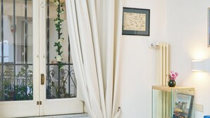 Une chambre à coucher avec un lit, une fenêtre avec des rideaux, une table de chevet avec une lampe et une étagère avec des livres et un vase.