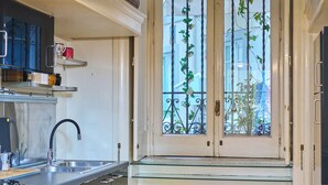 Une cuisine avec une fenêtre, un plancher en bois, un évier en acier inoxydable et quatre poubelles.