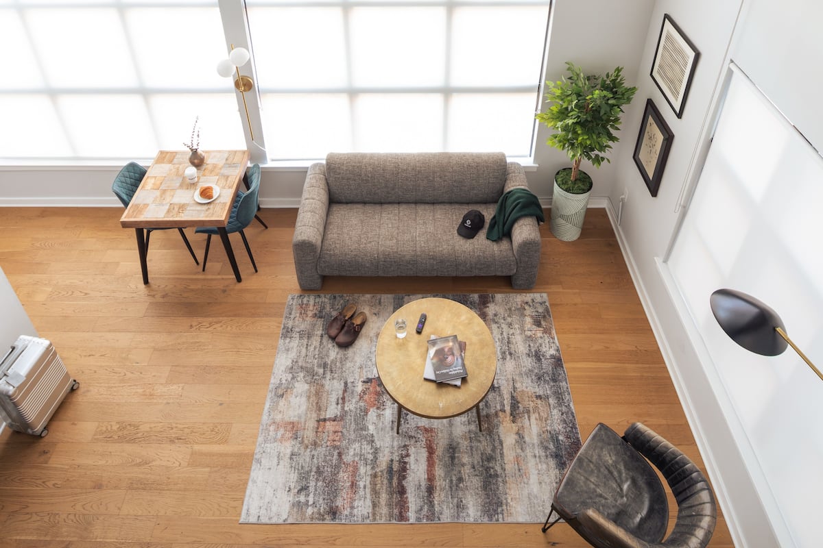 Ein modernes Wohnzimmer mit Holzboden, einem grauen Sofa, einem runden Couchtisch und einem Essbereich mit Holztisch und Stühlen.