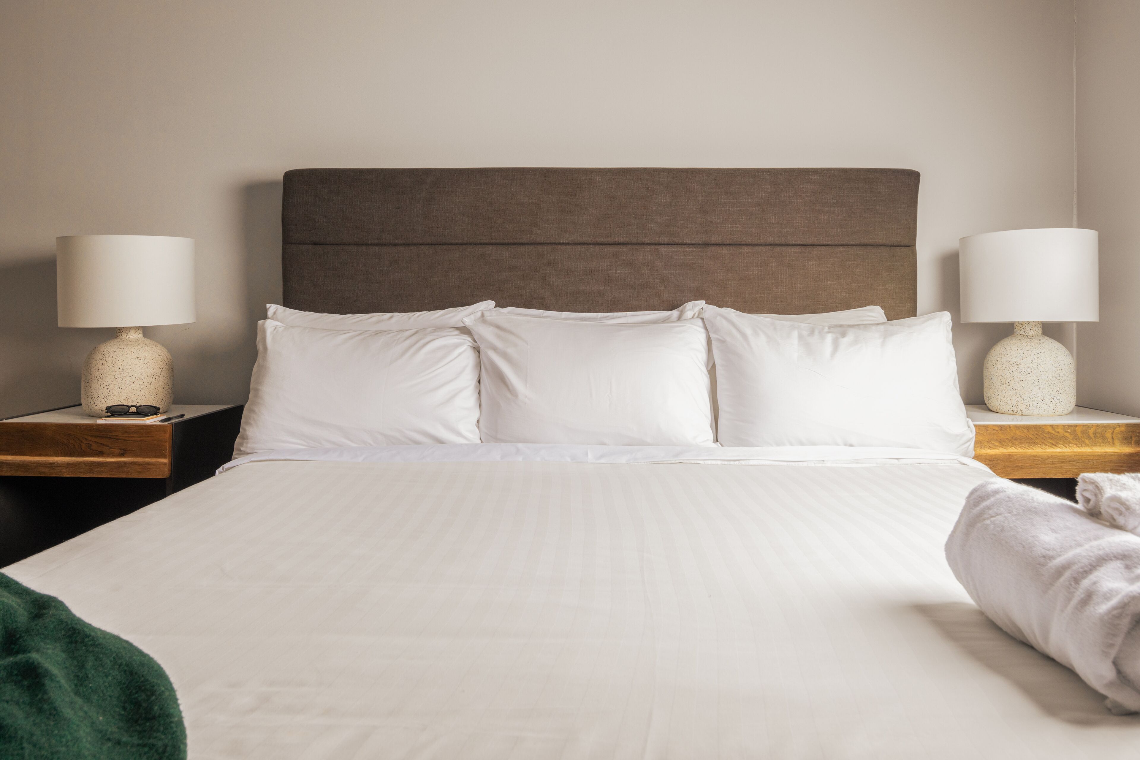 A neatly made bed with white linens, two bedside tables with lamps, and a green throw blanket on the floor.