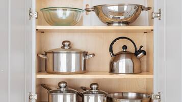 A kitchen cabinet with stainless steel cookware, including pots, a kettle, and a colander.