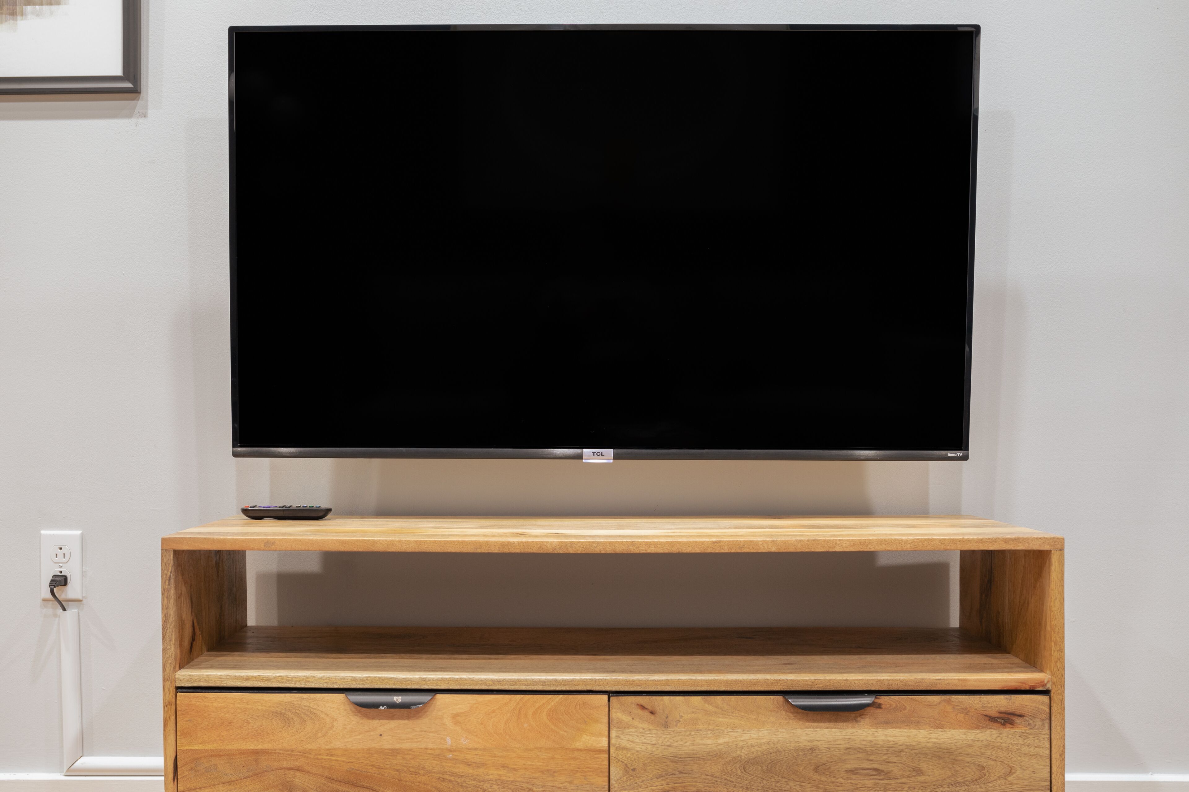 Una TV a schermo piatto montata su un mobile in legno con un cassetto sottostante.