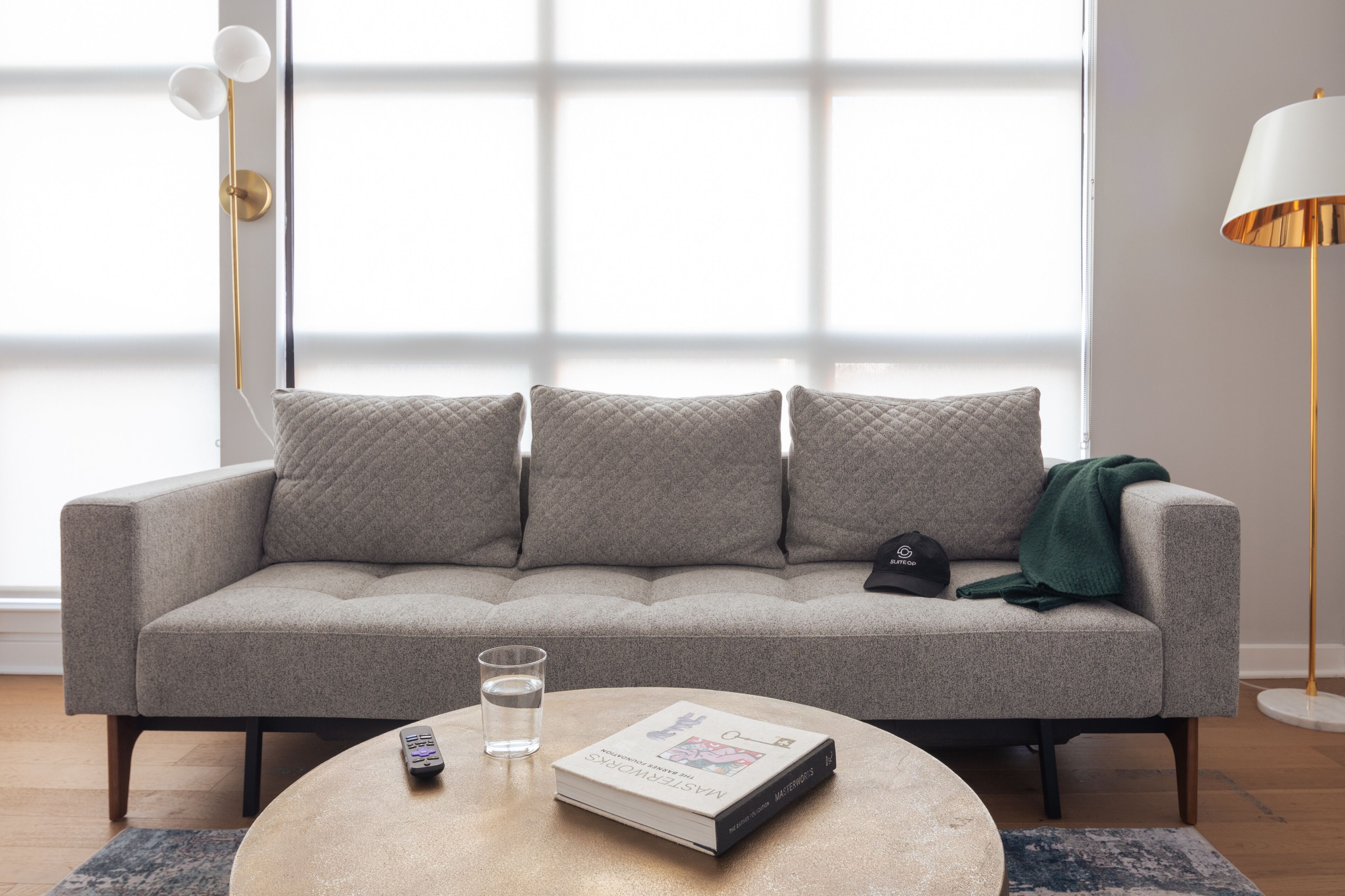 A modern living room with a grey sofa, a round coffee table, a remote control, a book, and a glass of water.