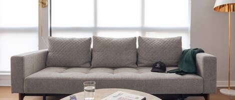A modern living room with a grey sofa, a round coffee table, a remote control, a book, and a glass of water.
