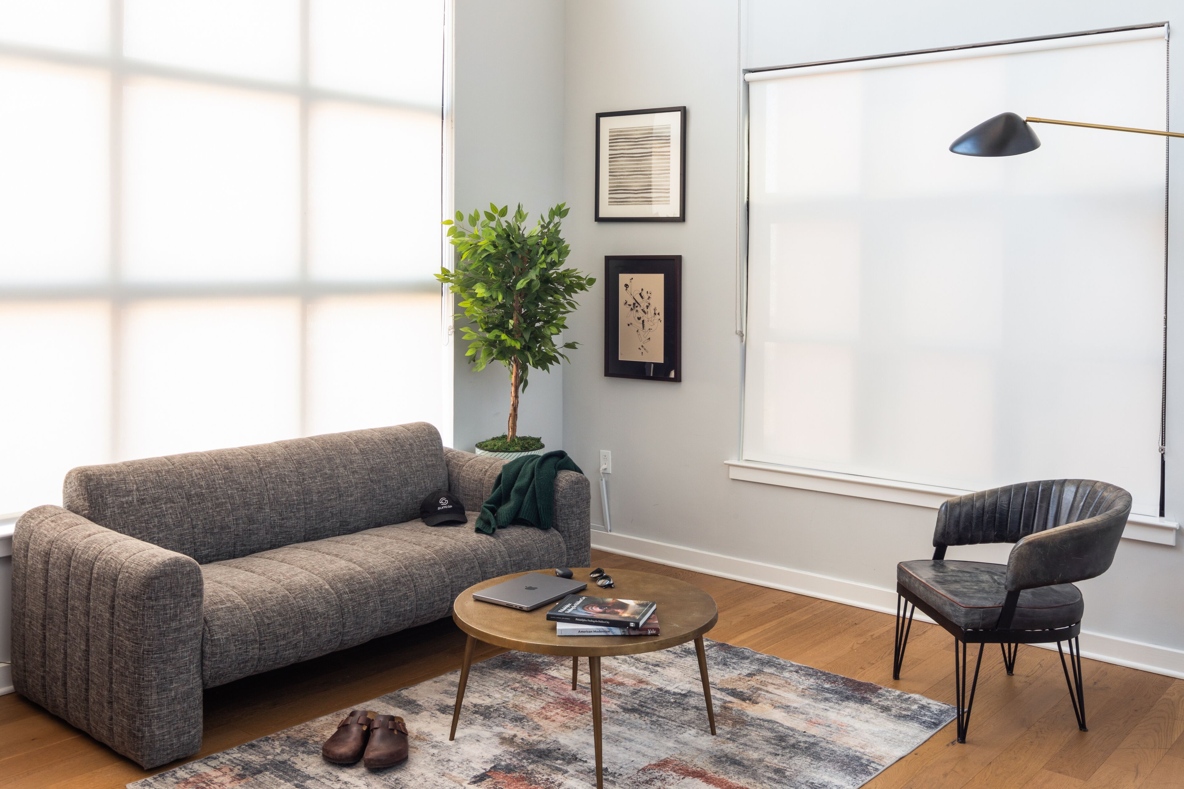 A living room with a grey sofa, a round coffee table, a black chair, a potted plant, and framed artwork on the wall.