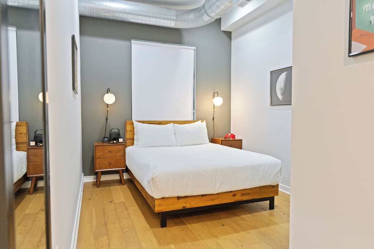 Ein Schlafzimmer mit einem hölzernen Bett, Nachttischen, einer Wandlampe und einem gerahmten Bild.