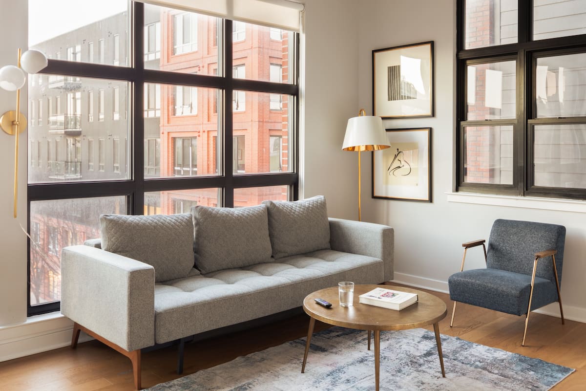 Ein modernes Wohnzimmer mit einem grauen Sofa, einem blauen Sessel, einem runden Couchtisch und einer Stehlampe.