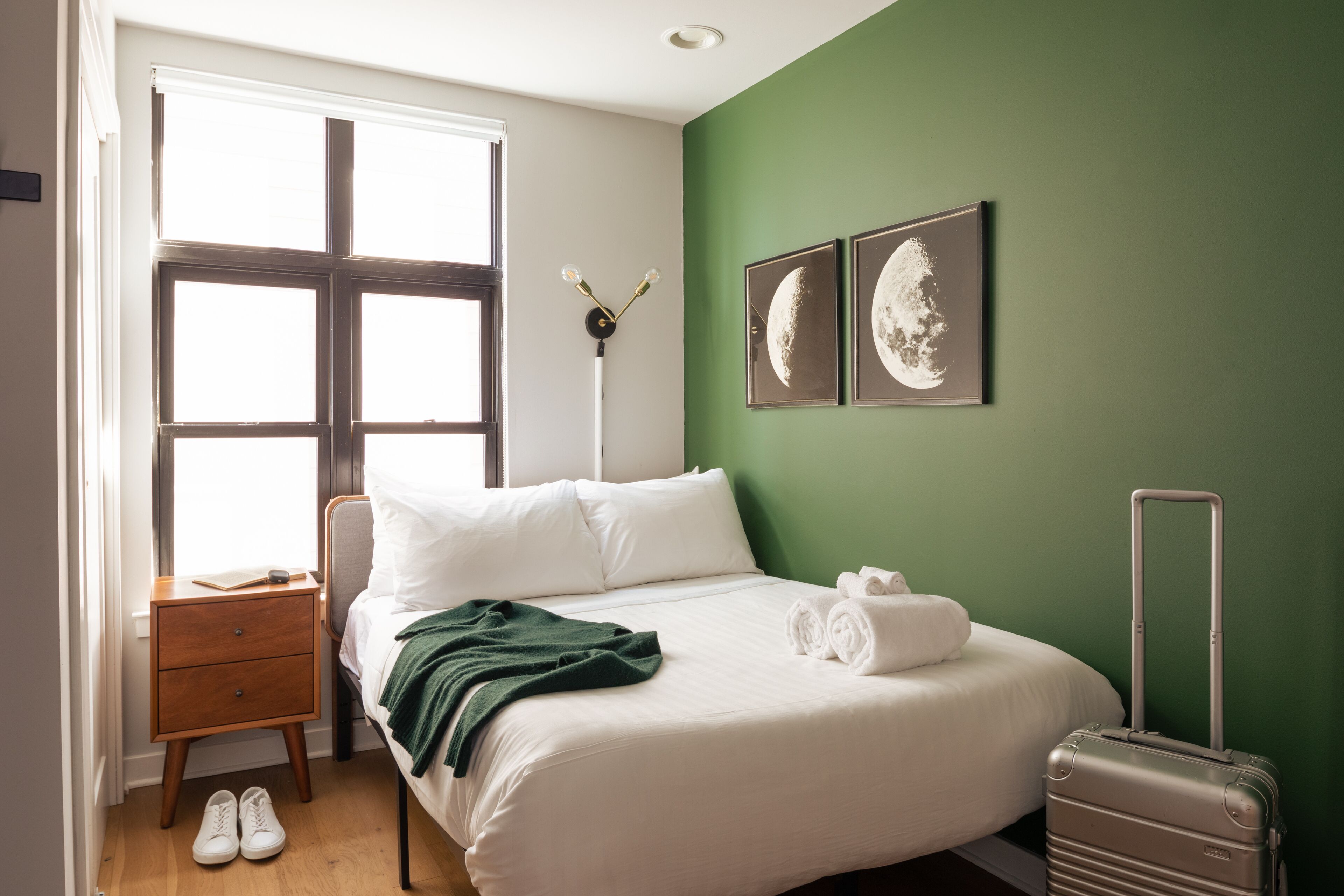 Ein ordentlich bezogenes Bett mit weißen Leinen, eine grüne Wand und zwei Bilder von Monden in Rahmen.
