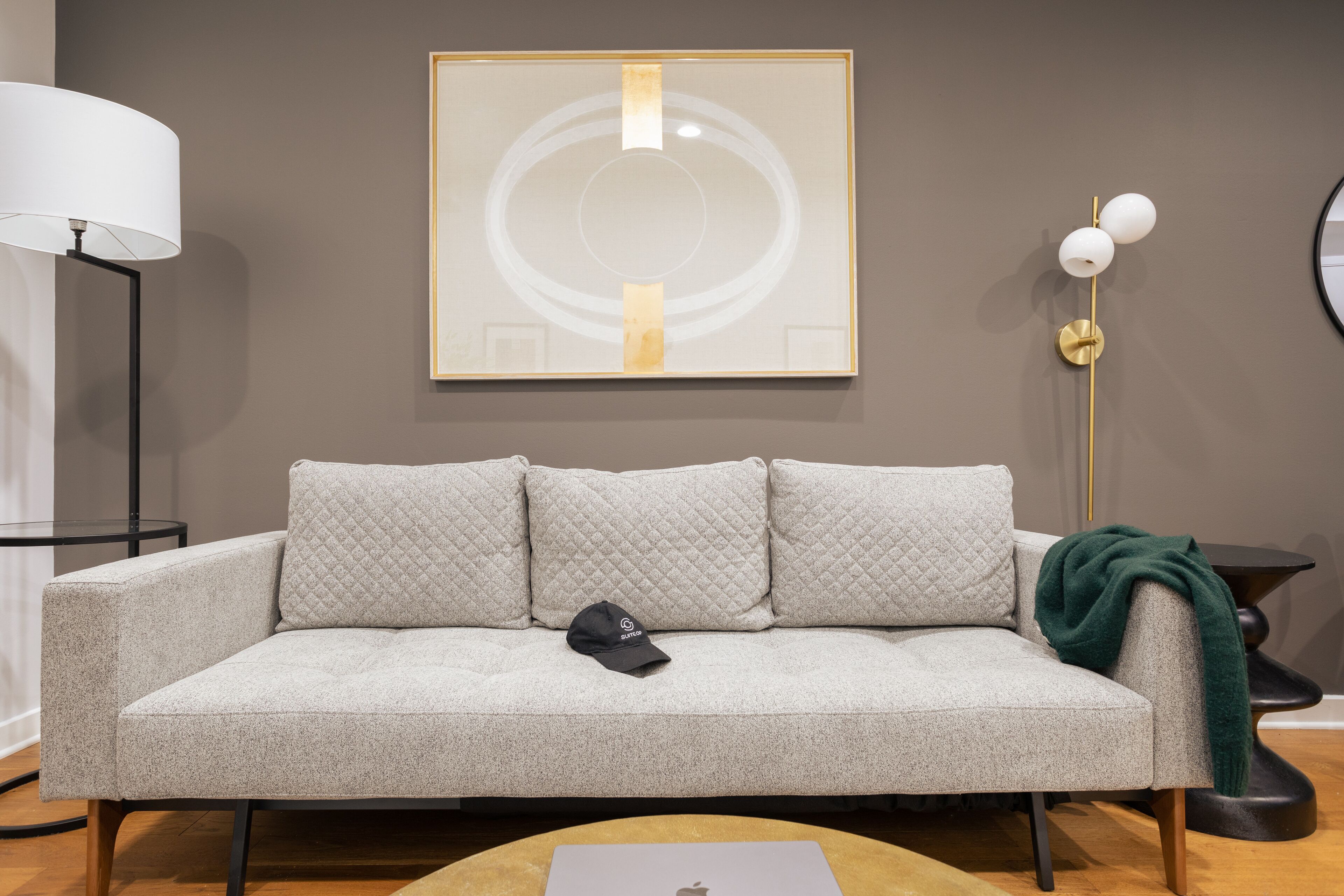 Un salon moderne avec un canapé gris, un tableau abstrait encadré, une lampe sur pied et une table d’appoint avec une lampe.