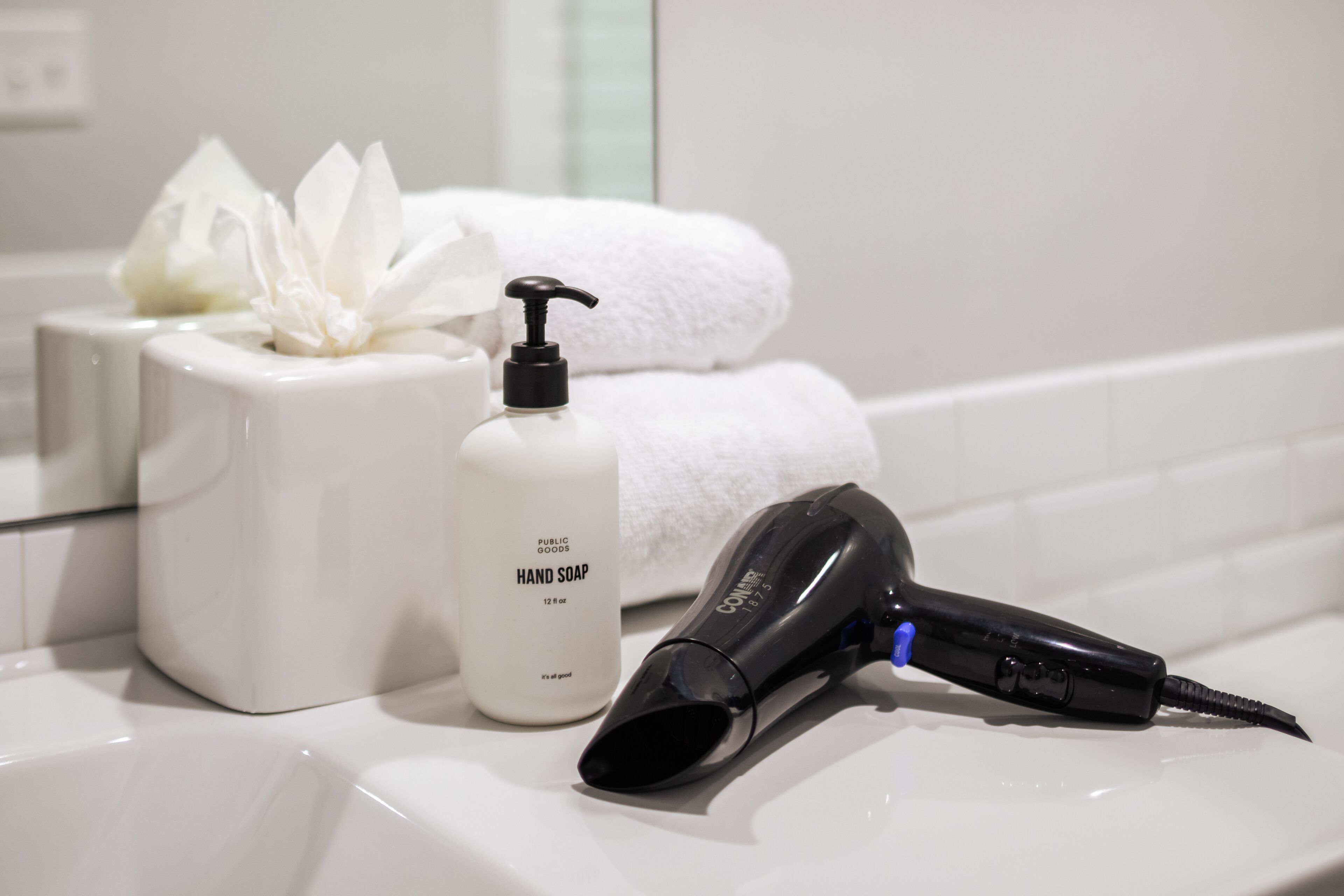 A bathroom with a white sink, a bottle of hand soap, a hairdryer, and a white towel.
