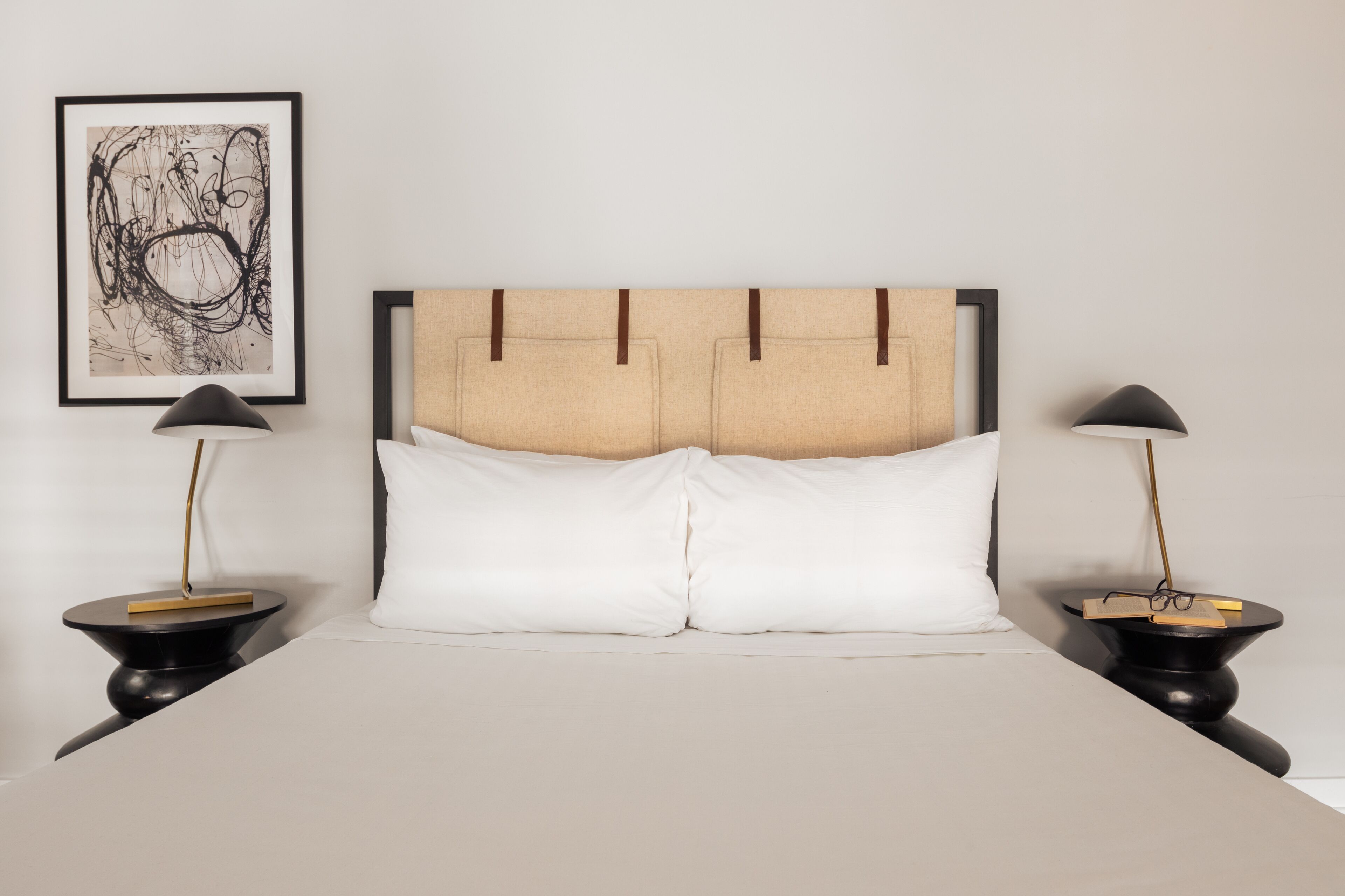 A neatly made bed with a headboard, two bedside tables, and a framed abstract artwork on the wall.