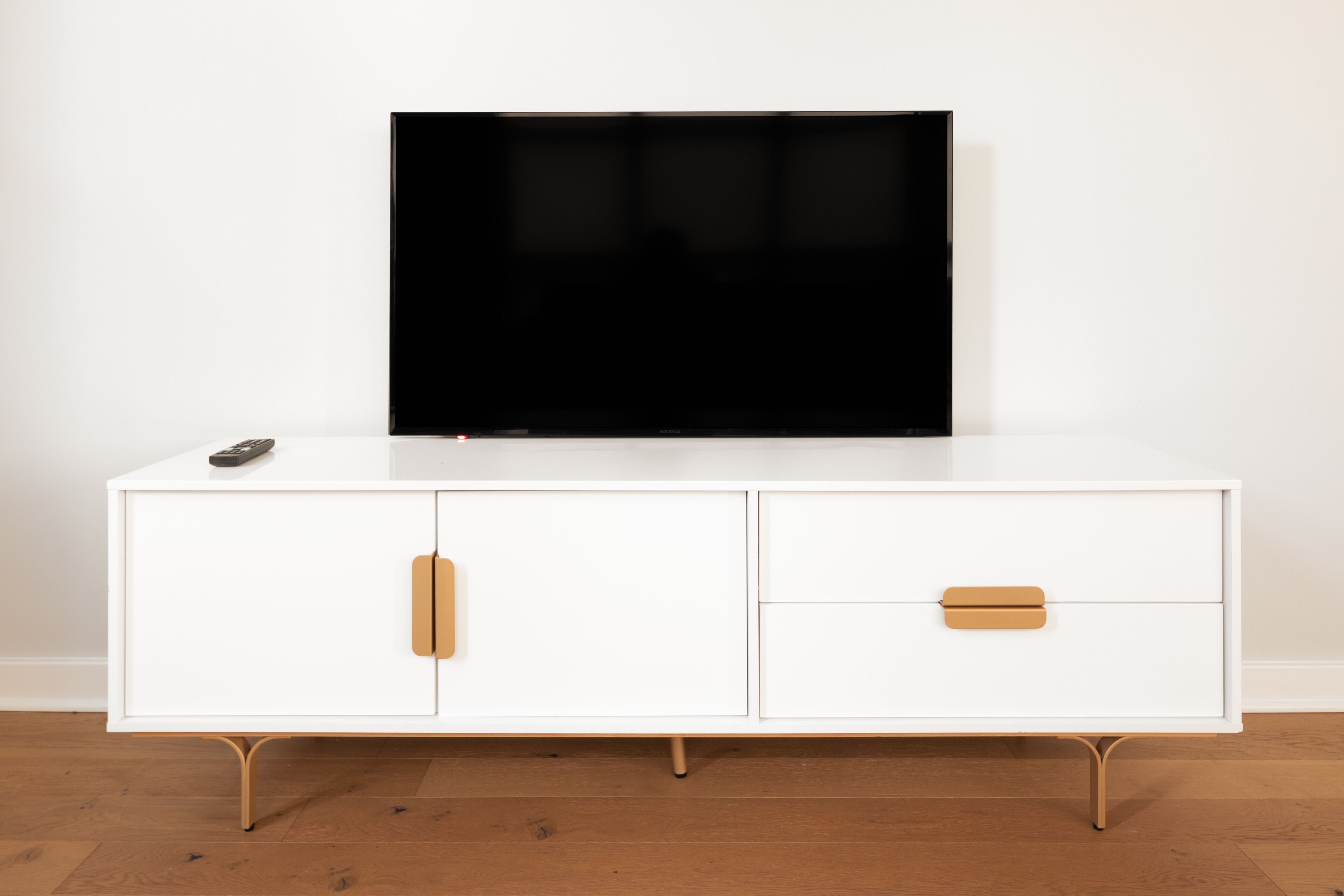 A white cabinet with a flat-screen TV on top, a remote control, and two wooden drawers.