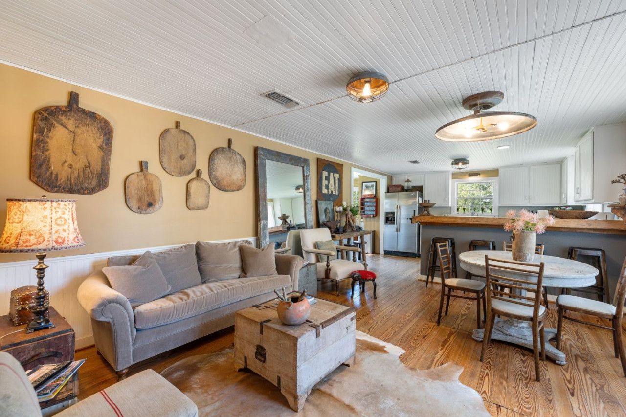 A cozy living room with a sofa, coffee table, and rustic decor. A kitchen area is visible in the background.