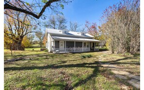 A single-story house with a porch, surrounded by trees and a grassy yard. - Fun, eclectic Round Top home w/POOL! 5 min to town (Fayette County)