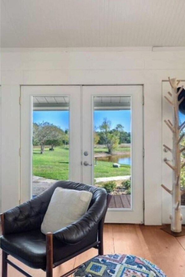 Une pièce avec un fauteuil en cuir noir, un tapis à motifs et une vue sur un jardin, visible à travers une porte vitrée.