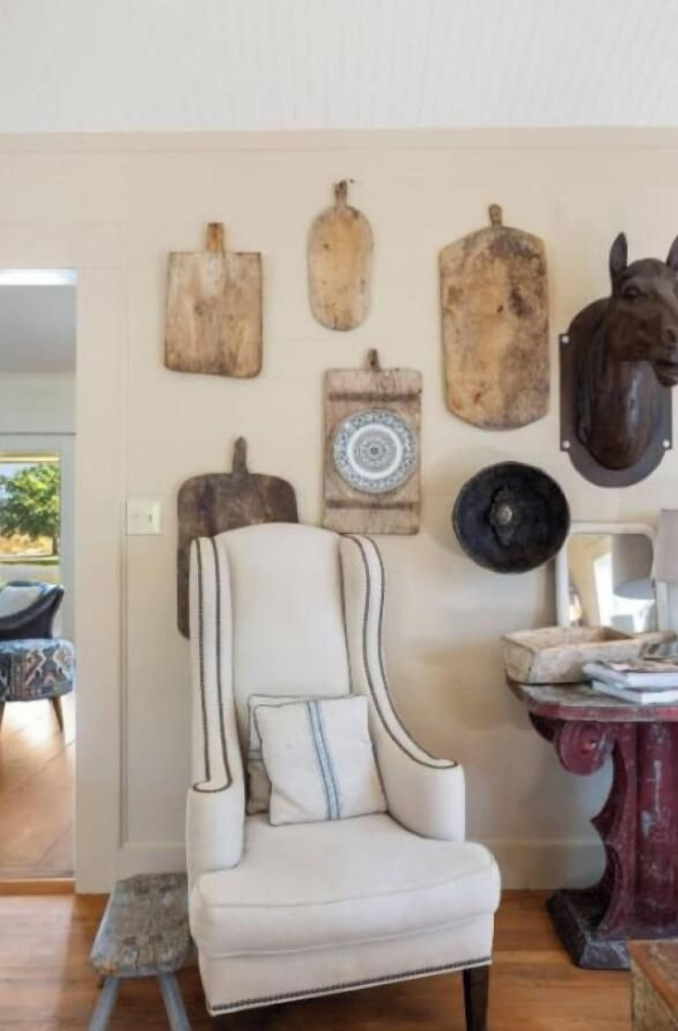 Een kamer met een witte fauteuil, een houten decoratie van een paardenhoofd en verschillende houten planken aan de muur.