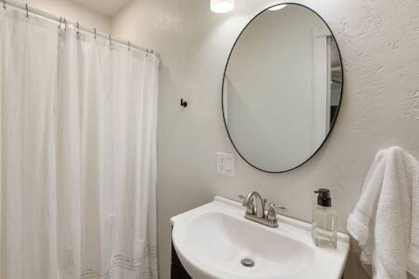 A bathroom with a white sink, a round mirror, and a shower curtain.