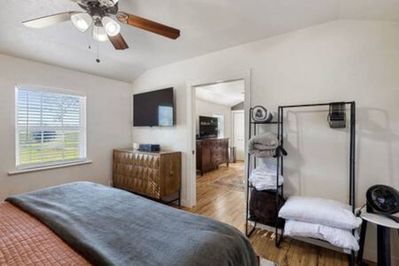 A bedroom with a bed, a wardrobe, a ceiling fan, a television, and a bathroom with a shower and a towel rack.