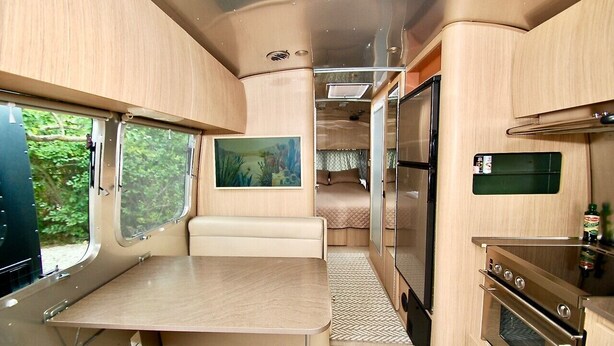 Een compact RV-interieur met een eethoek, kitchenette en een bed.