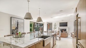 A modern kitchen with a marble island, pendant lights, and a built-in fireplace.