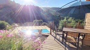 Un solarium in legno con piscina, circondato da fiori e con le montagne sullo sfondo.