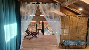 Una habitación con piso de madera, una mecedora, un banco con estampado tropical y una pared de piedra.