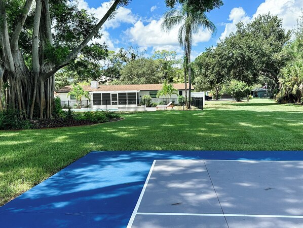 A residential area with a blue tennis court, a house with a garage, and a large tree.