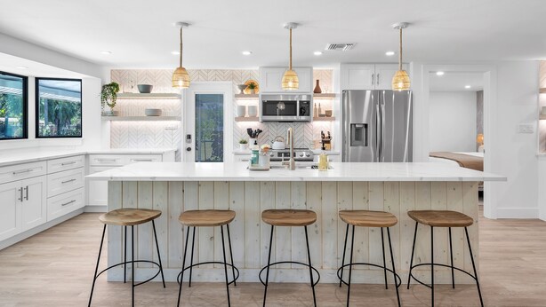 A modern kitchen with a large island, bar stools, and pendant lighting.